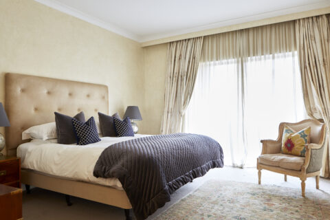 Period bedroom with king size bed dressed with navy blue cushions and blanket, armchair and doors leading out onto the balcony.