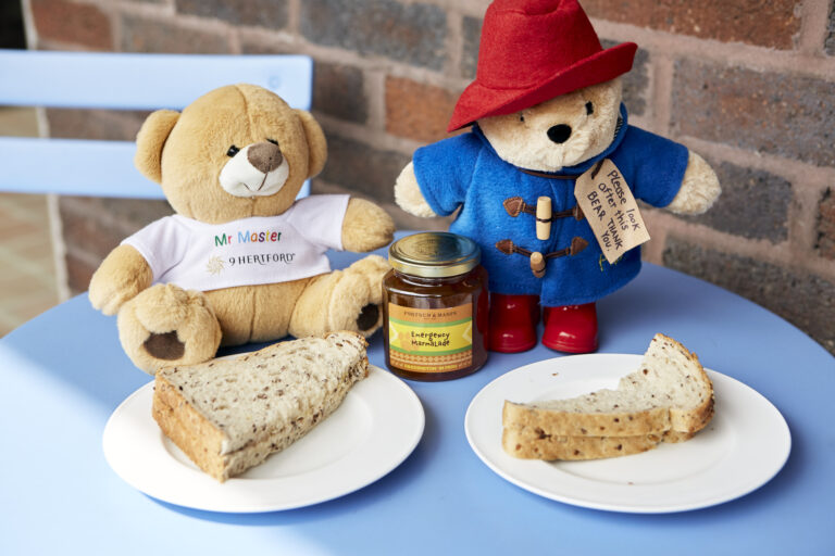 Mr Master (9 Hertford Street's teddy bear) and Paddington on a table, sharing a marmalade sandwich.