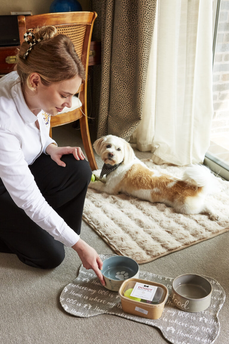 Dog on apartment floor next to concierge who is setting out pet bowls.