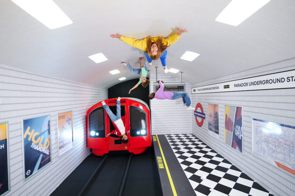 An area of the Paradox Museum in London which shows the recreation of a London underground station with a train, and visitors on the ceiling.