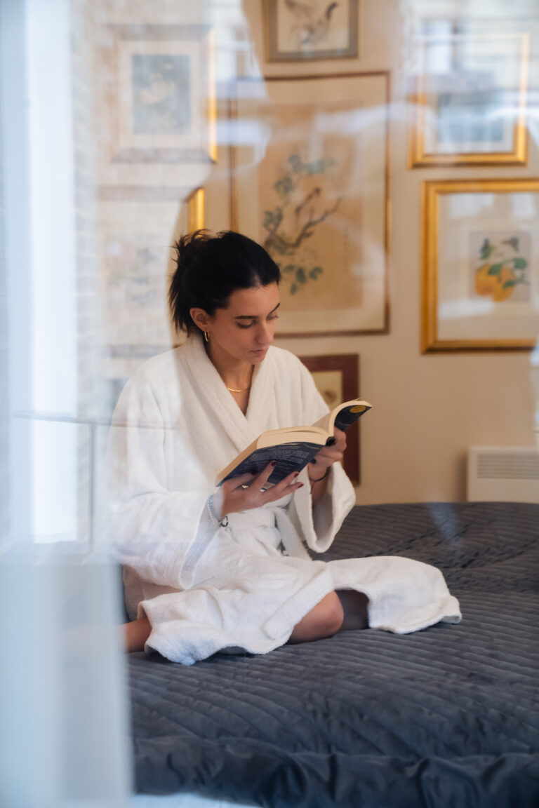 A guest sitting on the bed in her bathrobe, reading a book.