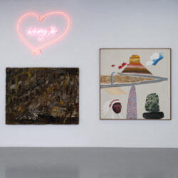 The white wall of the Saatchi Yates gallery for the exhibition Once Upon a Time in London, with a heart shaped neon sign, a dark painting and a light painting with bold colours and shapes.