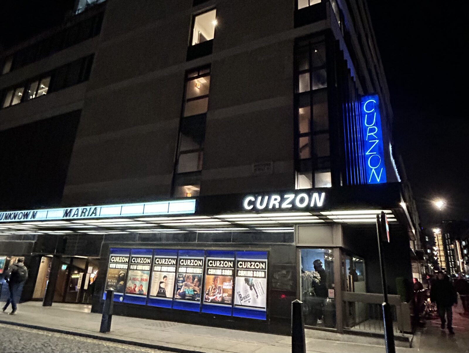 The exterior of the Curzon Mayfair at night, with period signage and blue neon 'Curzon' light.
