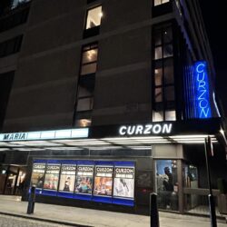 The exterior of the Curzon Mayfair at night, with period signage and blue neon 'Curzon' light.