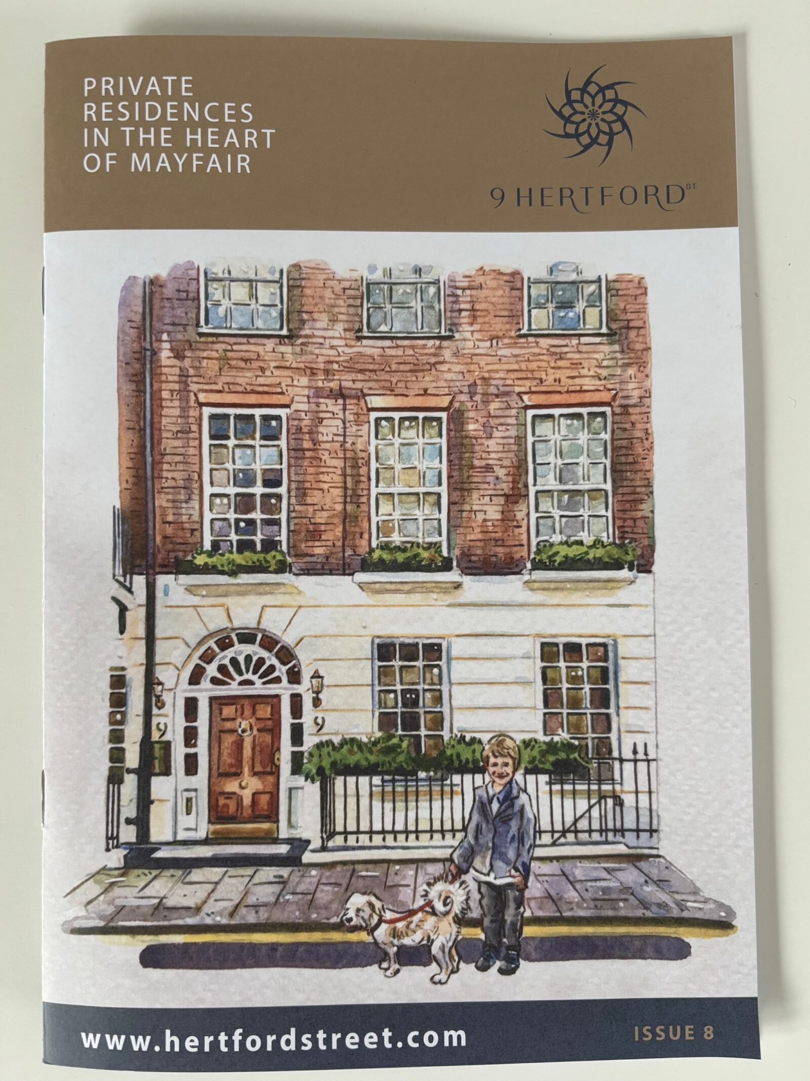 A photograph of the front of the 9 Hertford Street magazine, featuring an illustration of the Georgian brick and plaster facade of 9 Hertford Street, with a child and white dog in front of the building.