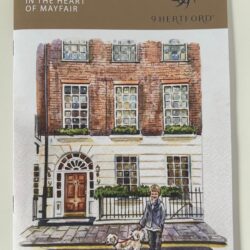A photograph of the front of the 9 Hertford Street magazine, featuring an illustration of the Georgian brick and plaster facade of 9 Hertford Street, with a child and white dog in front of the building.