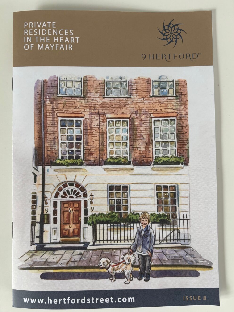 A photograph of the front of the 9 Hertford Street magazine, featuring an illustration of the Georgian brick and plaster facade of 9 Hertford Street, with a child and white dog in front of the building.