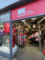 The entrance to a Crisis charity shop with open glass door, glass windows and a red shop sign.