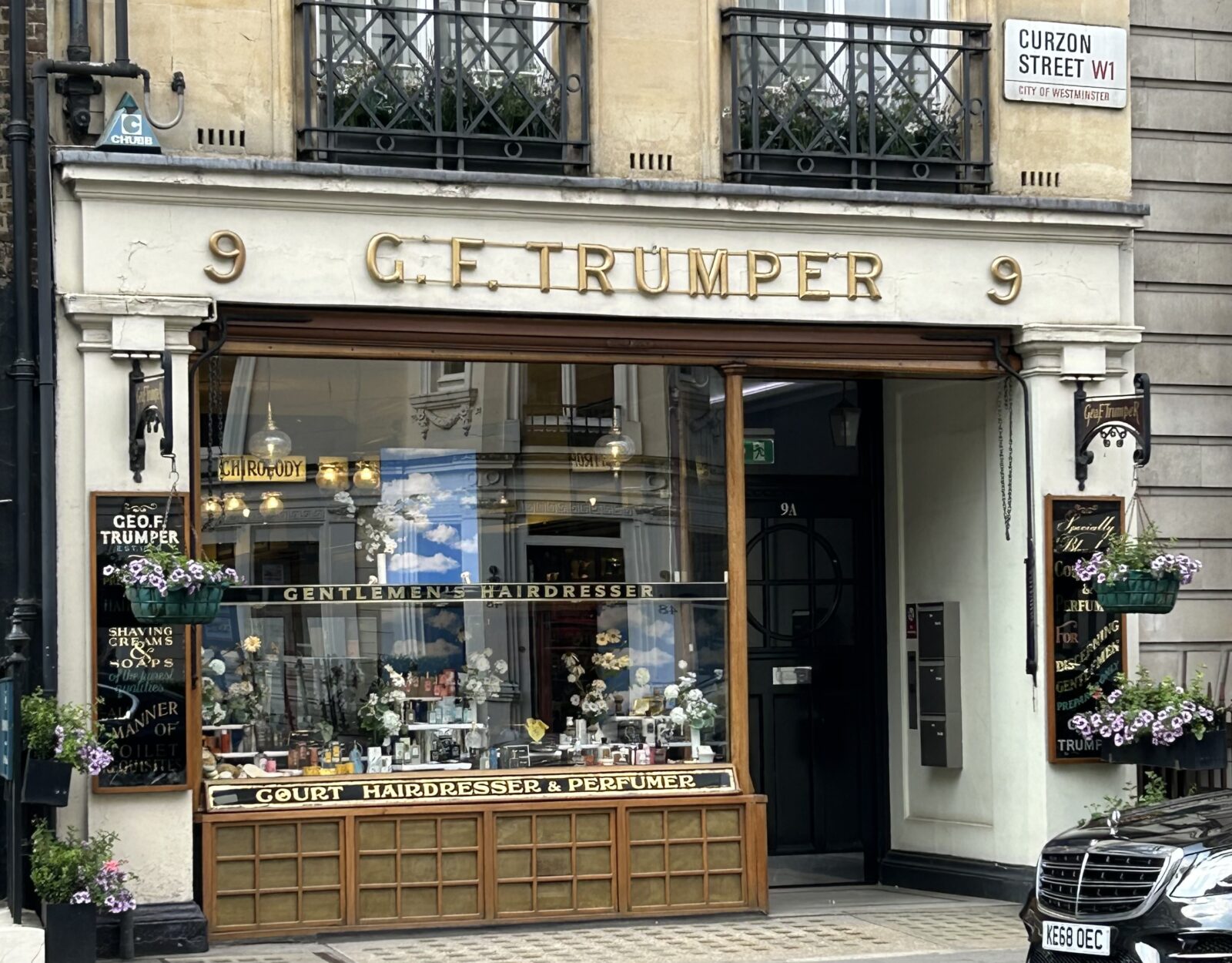 The exterior of Geo F Trumper on Curzon Street, London. It has a gold sign and the display in the window showcases its traditional grooming items and luxury toiletries.