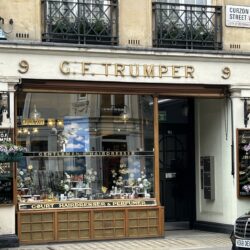 The exterior of Geo F Trumper on Curzon Street, London. It has a gold sign and the display in the window showcases its traditional grooming items and luxury toiletries.
