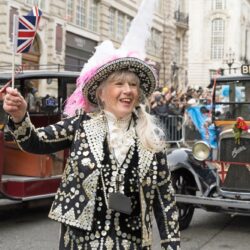 A pearly queen in traditional dress, with vintage cars behind her, at London's New Year's Day Parade.