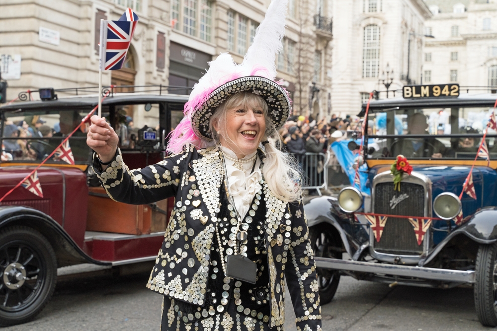 A pearly queen in traditional dress, with vintage cars behind her, at London's New Year's Day Parade.