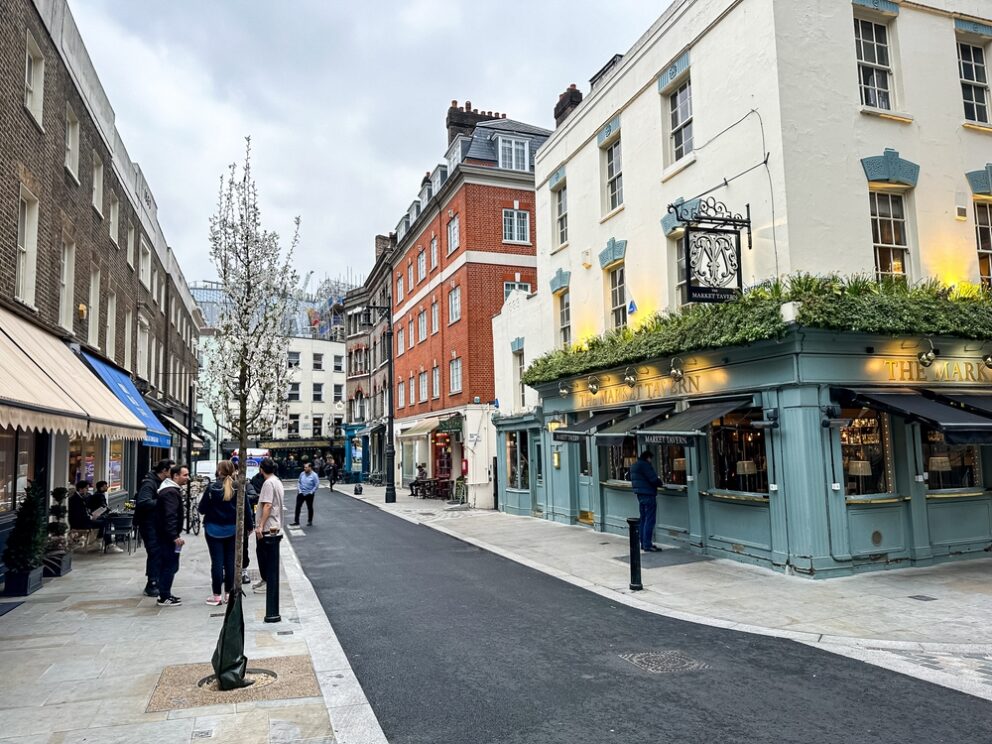 A street in Shepherd Market with canopied shops, a traditional pub and pedestrians.