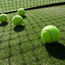 Four yellow tennis balls on a grass tennis court.