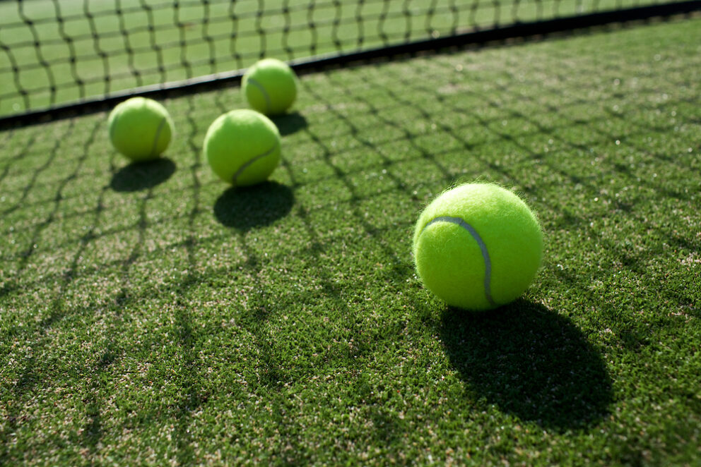 Four yellow tennis balls on a grass tennis court.
